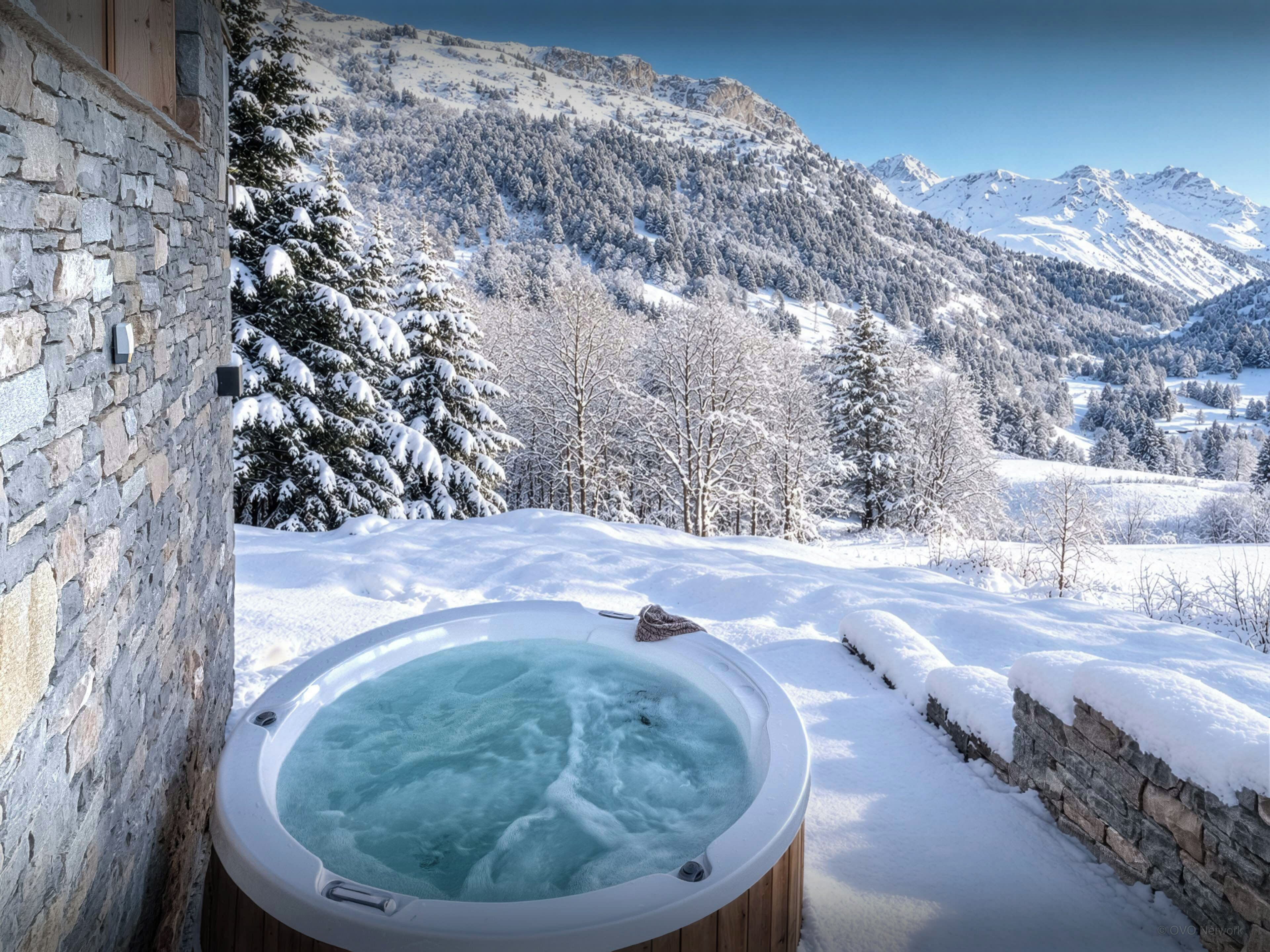 Un jacuzzi en un entorno nevado al aire libre, con montañas de fondo.