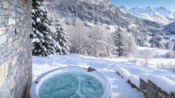 Un jacuzzi en un entorno nevado al aire libre, con montañas de fondo.