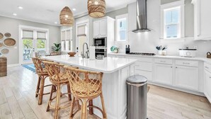 A modern kitchen with white cabinetry, a central island, wicker chairs, and pendant lighting. - Swaying Palms by Stay on 30a (Inlet Beach)