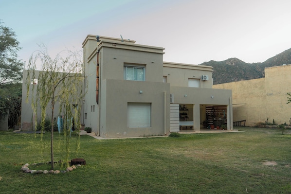 A modern two-story building with a garage, a small garden with a tree, and a mountain in the background.