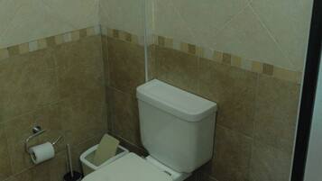 A bathroom with a toilet, bidet, and a roll of toilet paper on the floor.
