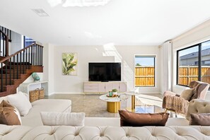 Un salon moderne avec un canapé, une table basse, un téléviseur et un escalier.