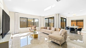 A spacious living room with a large sofa, a coffee table, and a dining area with chairs. - Stunning Park-fronted Luxury Grand Family House with Gym, Pool and Spa!!! (Mambourin)