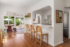 Una cocina moderna con muebles blancos, un refrigerador de acero inoxidable y un comedor con sillas y una mesa de madera.