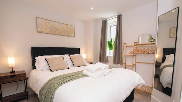 A neatly arranged hotel room with a bed, bedside tables, a mirror, and a window with curtains. - Stylish 1BR Sanctuary in Hull Centre Near Marina (Kingston upon Hull)