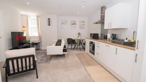 A modern living room with a sofa, a black chair, a TV, and a dining area with a table and chairs. - Stylish 1BR Sanctuary in Hull Centre Near Marina (Kingston upon Hull)