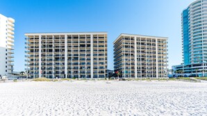 A beachfront hotel with multiple floors, balconies, and a sandy beach in the foreground. - The Palms East 901 | Beachfront | Pools | My Beach Getaways (Orange Beach)