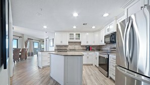 A modern kitchen with white cabinets, a stainless steel refrigerator, and a central island. - The Palms East 901 | Beachfront | Pools | My Beach Getaways (Orange Beach)