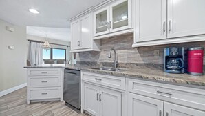 A modern kitchen with white cabinetry, a granite countertop, a built-in dishwasher, and a coffee maker. - The Palms East 901 | Beachfront | Pools | My Beach Getaways (Orange Beach)
