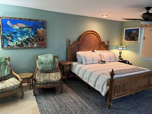 A bedroom with a bed, two chairs, a round side table, a wooden headboard, a rug, and two wall-mounted paintings. - Water front 5-bedroom house with boat dock in beautiful Marathon (Marathon)