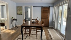 Un comedor con una mesa y sillas de madera, una alfombra, una puerta corrediza y vistas amplias a través de grandes ventanales.