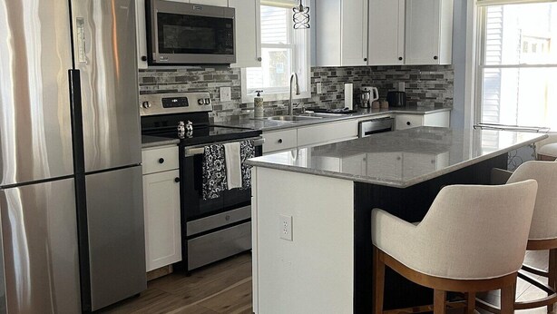 Una cocina moderna con electrodomésticos de acero inoxidable, una isla central e iluminación colgante.