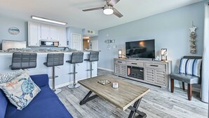 En moderne stue med sofa, sofabord, fjernsyn og et køkkenområde med barstole.