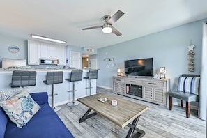 A modern living room with a sofa, a coffee table, a TV, and a kitchen area with bar stools. - The Turquoise Turtle, Sleeps 4 with Stunning Oceanview. New Pools! (Galveston)