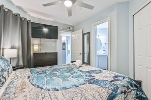 A bedroom with a bed, a ceiling fan, a TV, and a door leading to a bathroom. - The Turquoise Turtle, Sleeps 4 with Stunning Oceanview. New Pools! (Galveston)