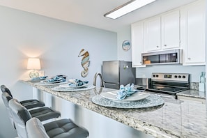 A modern kitchen with a marble countertop, stainless steel appliances, and a unique wall art piece. - The Turquoise Turtle, Sleeps 4 with Stunning Oceanview. New Pools! (Galveston)
