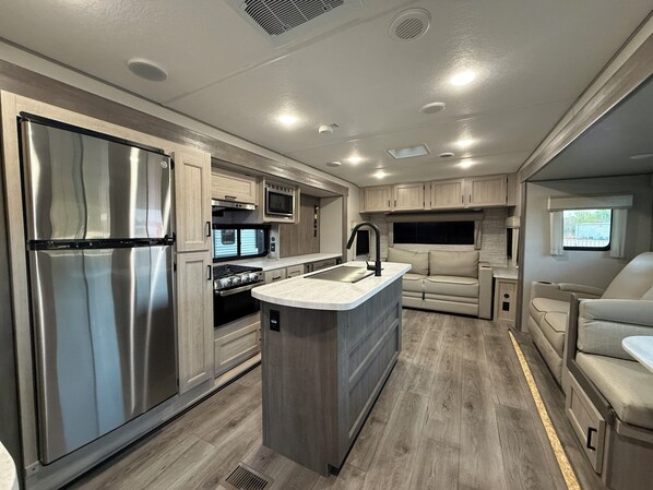 A compact RV kitchen with a refrigerator, stove, microwave, and sink. - Peaceful 1-bedroom recreational vehicle with AC in Flint unit 2 (Flint)