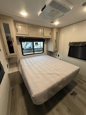 A compact RV interior with a bed, a window, and built-in cabinets. - Peaceful 1-bedroom recreational vehicle with AC in Flint unit 2 (Flint)
