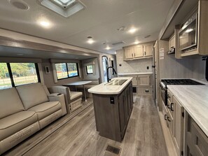 A compact RV kitchen with a central island, a dining area with a table and chairs, and a seating area with a sofa. - Peaceful 1-bedroom recreational vehicle with AC in Flint unit 2 (Flint)