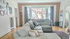 Ein Wohnzimmer mit Ecksofa, Deckenventilator und großem Fenster mit Vorhängen.