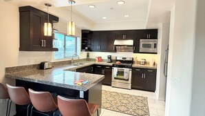 A modern kitchen with dark cabinets, a central island, bar stools, a microwave, and a stove.
