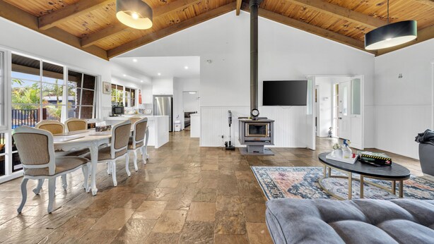 A spacious living area with a high ceiling, a fireplace, a dining table with chairs, and a sofa.