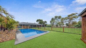 A swimming pool with artificial grass, a fenced area, and a building in the background.