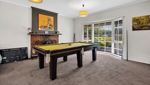 A pool table in a room with a fireplace, large windows, and artwork on the walls.
