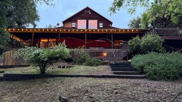 A wooden cabin with a covered porch, outdoor seating, and a staircase leading to a deck.