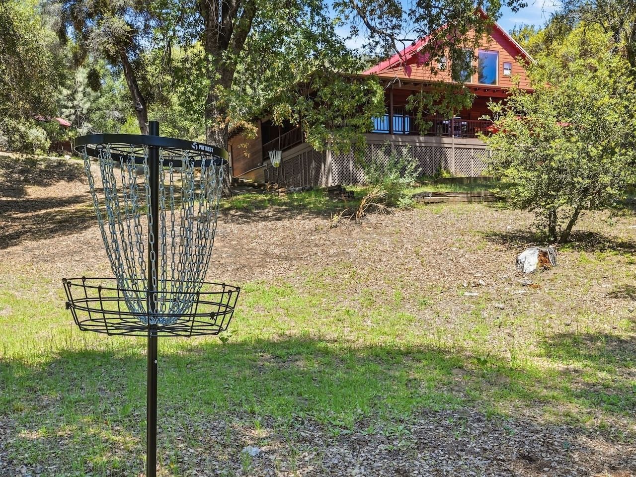 A disc golf basket in a grassy area with a wooden house in the background.