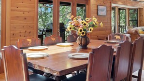 A wooden dining room with a large table, chairs, and a vase of sunflowers.