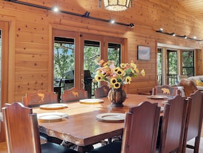 Une salle à manger en bois avec une grande table, des chaises et un vase rempli de tournesols.