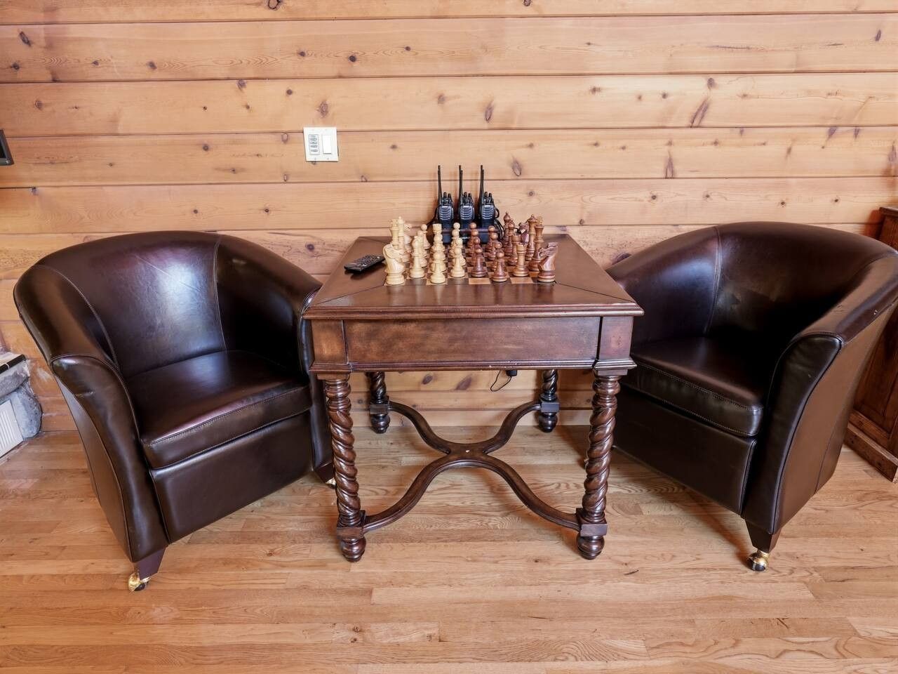 A wooden table with chess pieces in the center, flanked by two leather chairs.