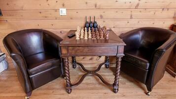 A wooden table with chess pieces in the center, flanked by two leather chairs.