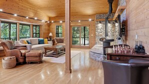 A spacious living room with a fireplace, wooden floors, and large windows.