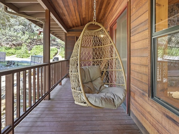 A wooden deck with a hanging chair and a view of the outdoors.