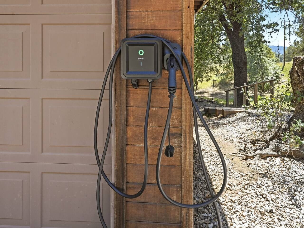 An EV charging station mounted on a wooden post, connected to a garage door.