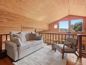 A cozy cabin interior with a sofa, chair, and a view of the outdoors through a window.