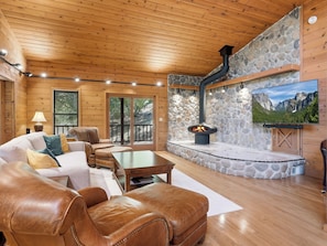 L’intérieur chaleureux d’un chalet avec une cheminée en pierre, des meubles en cuir et un téléviseur fixé au mur.