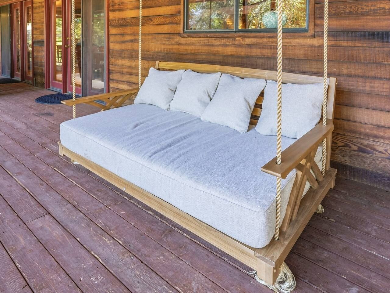 A wooden deck with a single mattress on a swing bed.