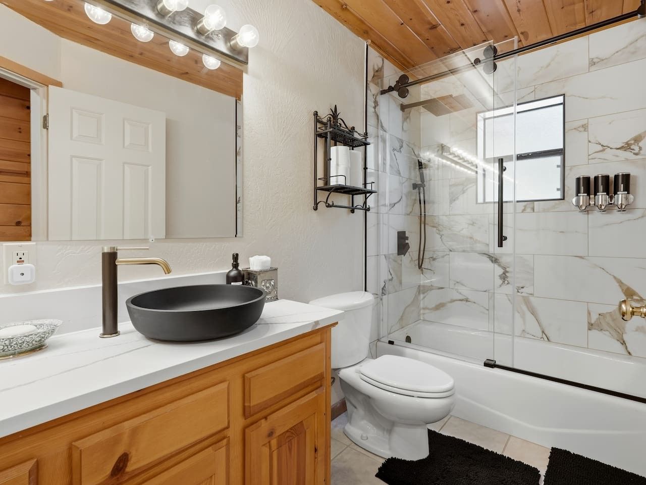 A bathroom with a large mirror, a black vessel sink, a toilet, and a glass-enclosed shower area.