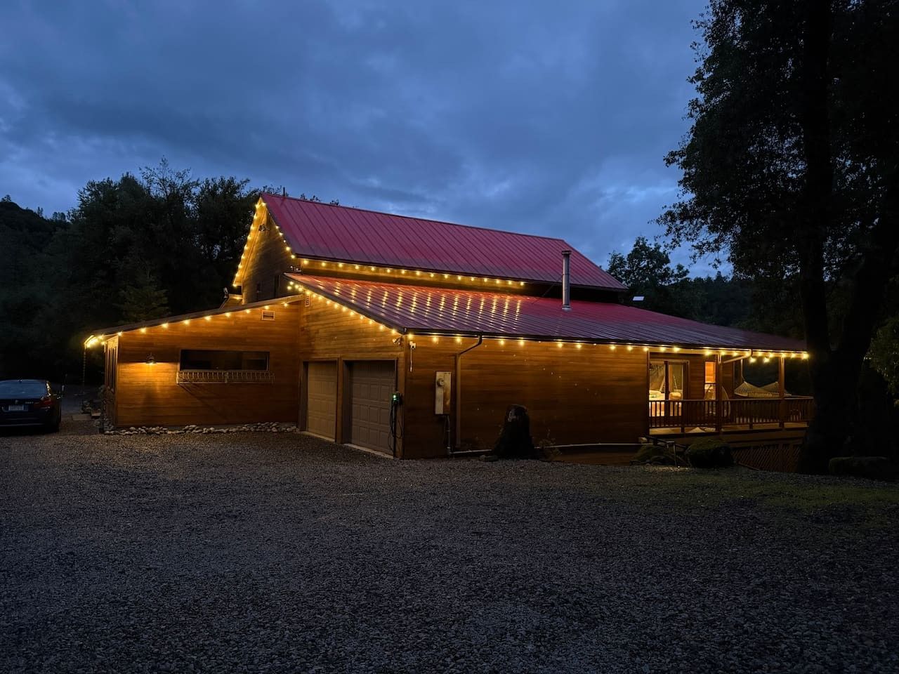 A wooden building with a red roof and string lights, a covered porch, and a gravel driveway.