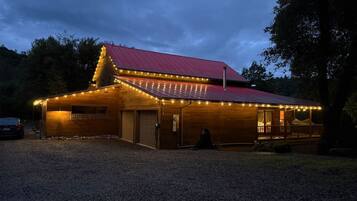 A wooden building with a red roof and string lights, a covered porch, and a gravel driveway.
