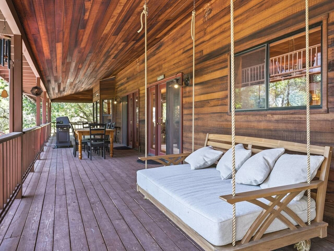 A wooden deck with a swing bed, outdoor furniture, and a grill.