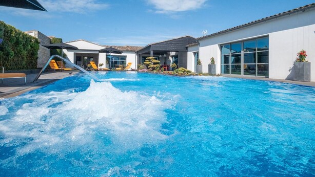 En swimmingpool med vandrutsjebaner, omgivet af moderne bygninger med store vinduer og en klar himmel.