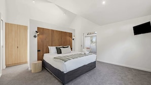 Ein modernes Schlafzimmer mit einem großen Bett, einem Holz-Kopfende, einem kleinen Nachttisch, einem an der Wand montierten Fernseher und einer Schiebetür.