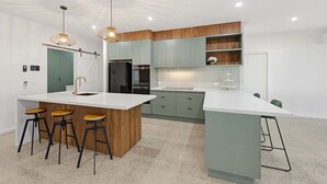 Eine moderne Küche mit einer zentralen Kochinsel, Barhocker, einem Kühlschrank und einem Einbauofen.