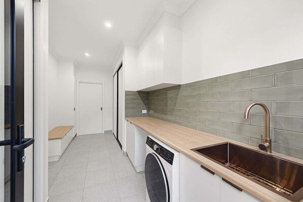 A compact kitchen with a washing machine, a sink with a modern faucet, and a tiled backsplash.