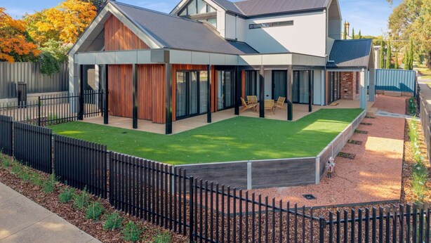 Ein modernes, zweistöckiges Haus mit überdachter Terrasse, umzäunter Garten und gepflegtem Rasen.