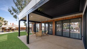 Eine moderne Außenpatio mit einer überdachten Sitzgruppe, einem Rasen und Blick auf ein Hotel im Hintergrund.